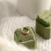 14K yellow gold birthstone stackable rings with 2mm round stones on a green velvet box, white fabric, and green plant in the background.
